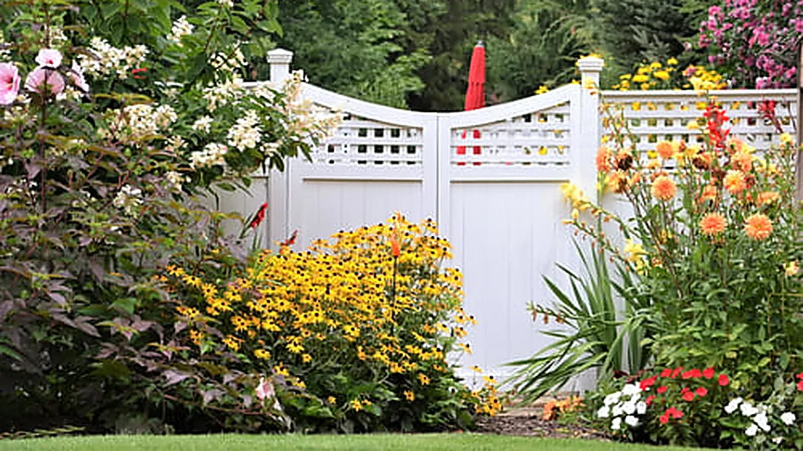 New white vinyl privacy fence installed beside a colorful landscaped garden bed
